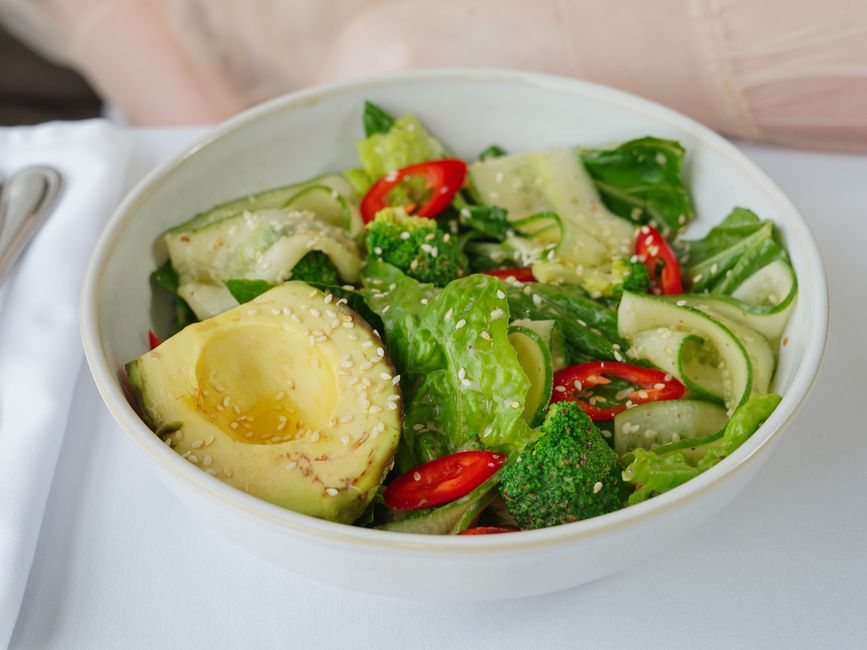 Fresh vegetable salad in a white bowl with avocado and sesame seeds